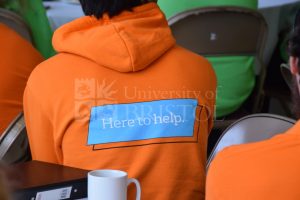 Student wearing bright orange hoodie that reads: here to help